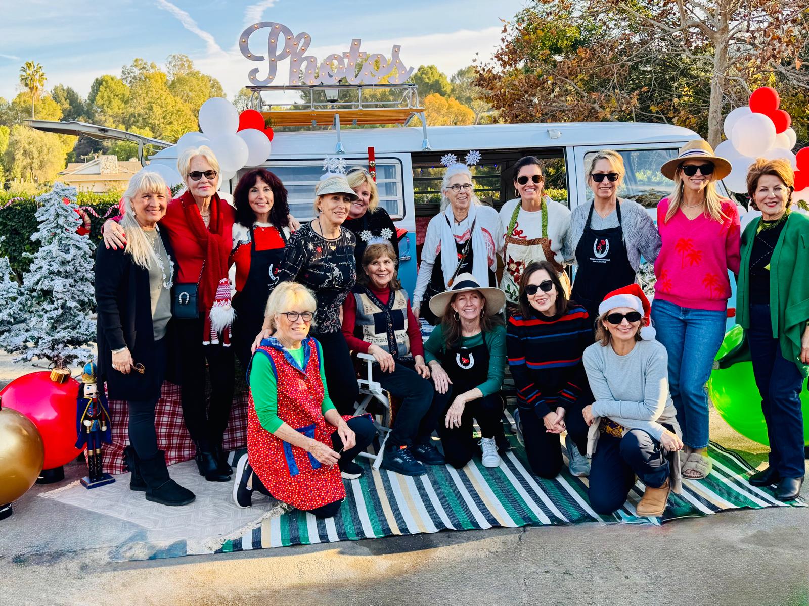 Large group of women from a community club posing together in front of the holiday-decorated Photobus