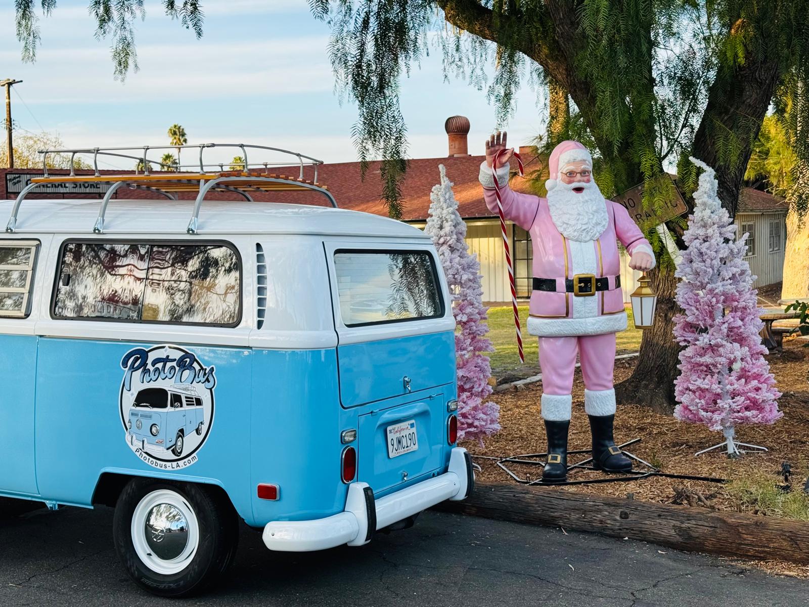 Rear three-quarter view of the 1970 VW Photobus beside a pink Santa statue and flocked pink Christmas trees